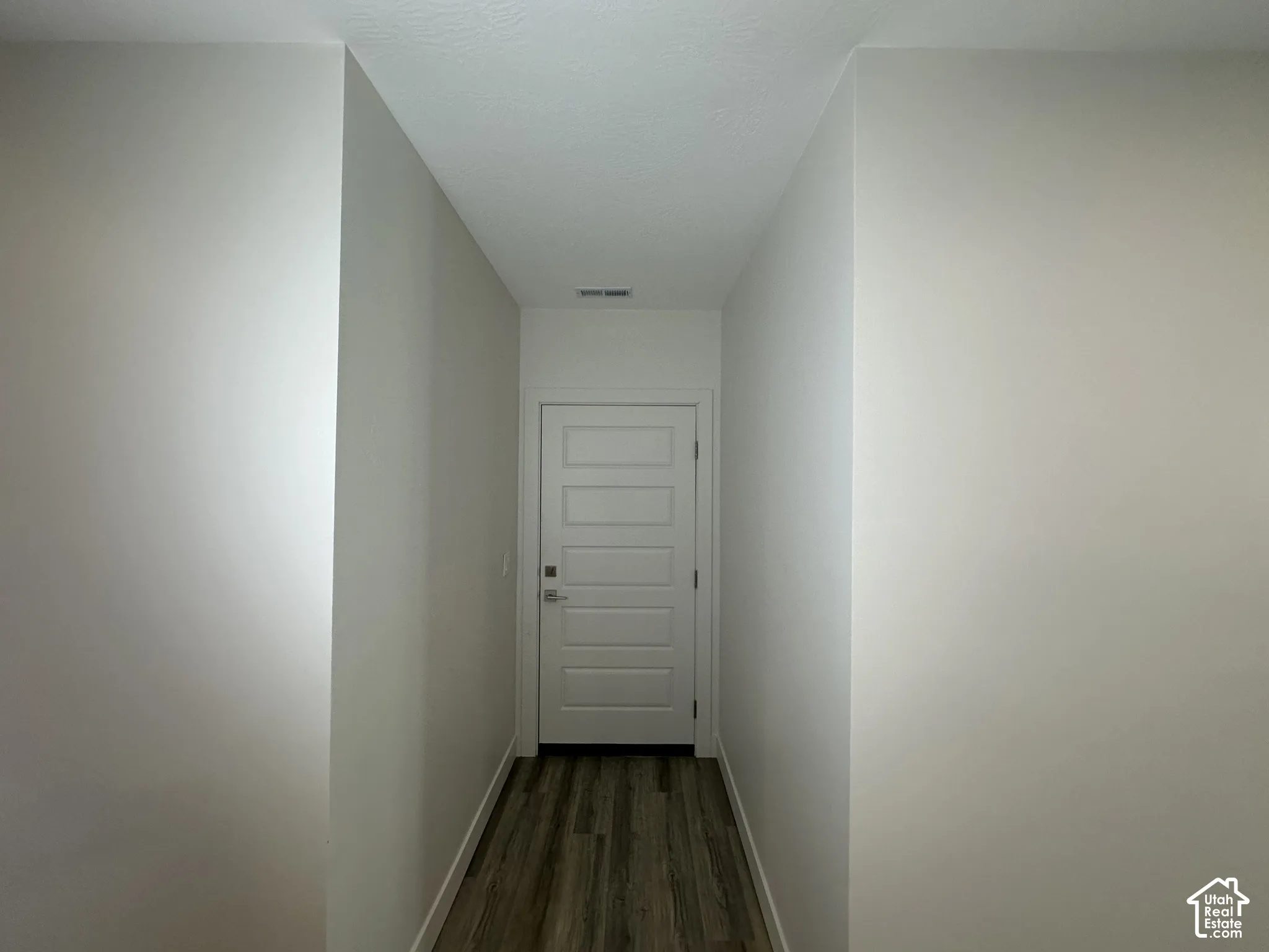 Hallway featuring wood-finish flooring, light neutral wall paint, and a five-panel interior door