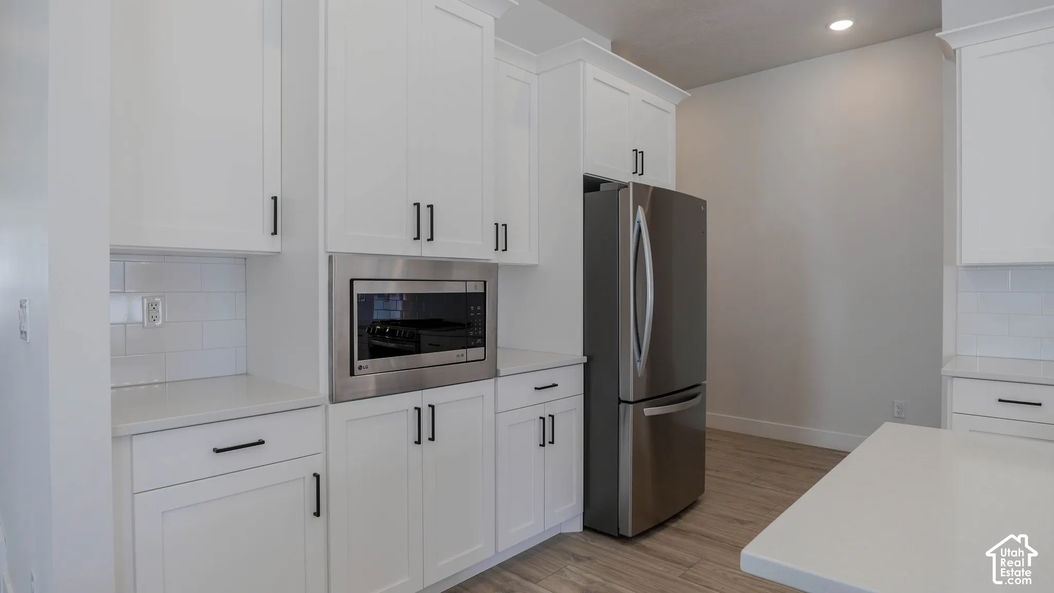 Kitchen featuring white shaker cabinetry, stainless steel appliances, light countertops, subway tile backsplash, and wood-finish flooring