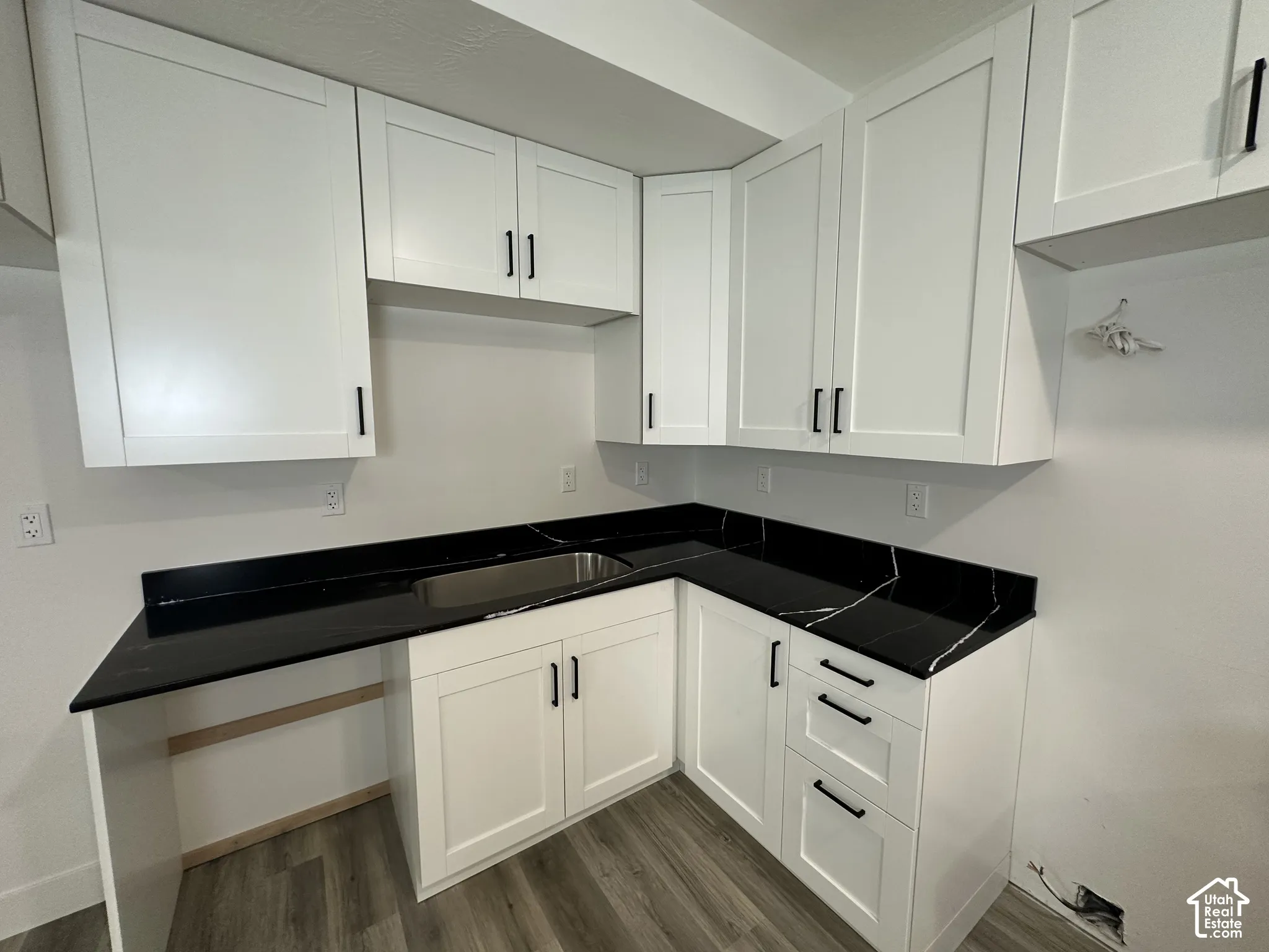 White shaker-style cabinetry with matte black hardware, dark countertops with white veining, integrated stainless steel sink, and wood-finish flooring
