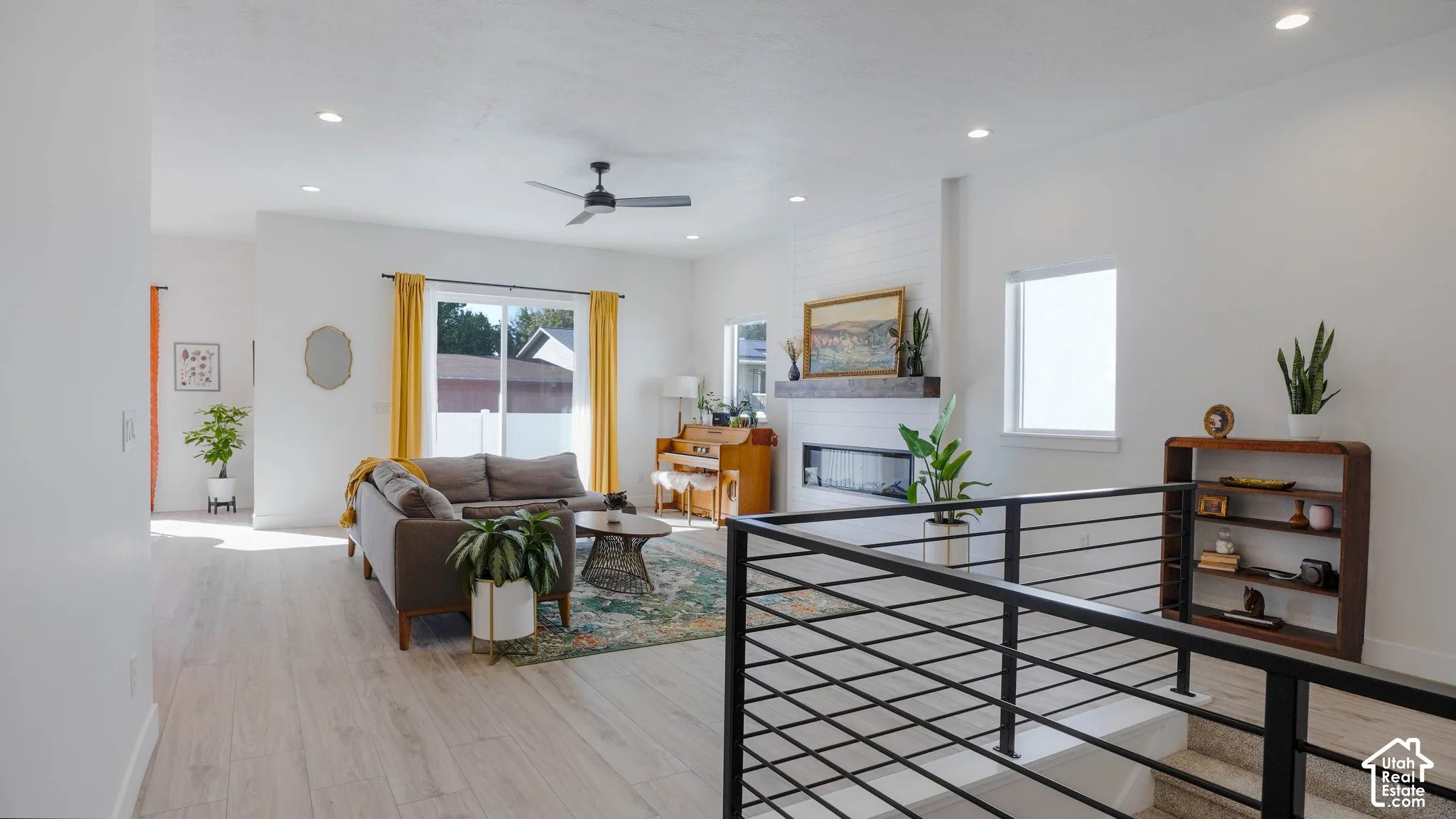 Contemporary open-concept living area featuring light wood-finish flooring, recessed lighting, and a modern fireplace with a wood mantel