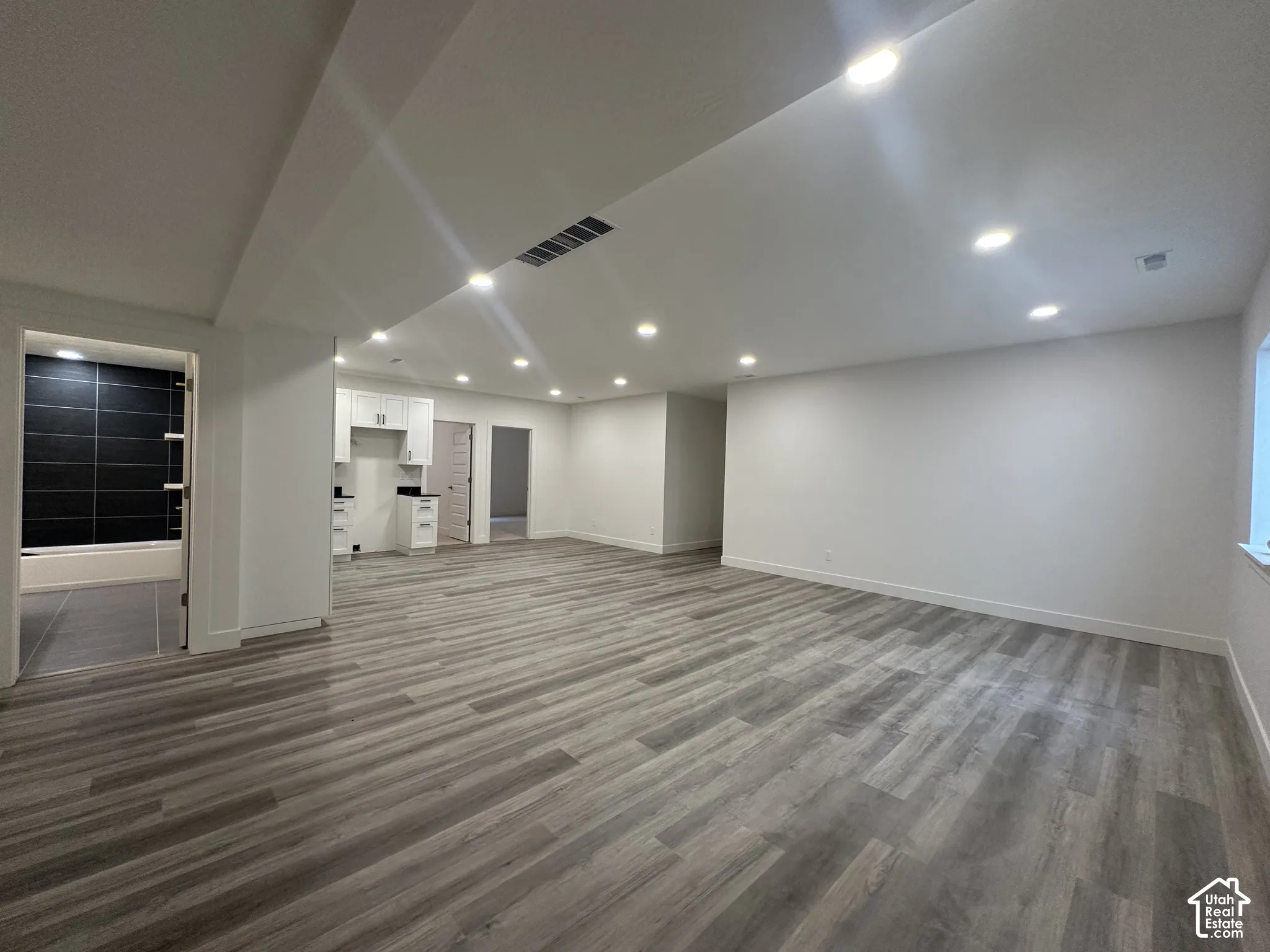 Spacious interior featuring wood-finish flooring, recessed lighting, and a white cabinet kitchenette with a dark countertop