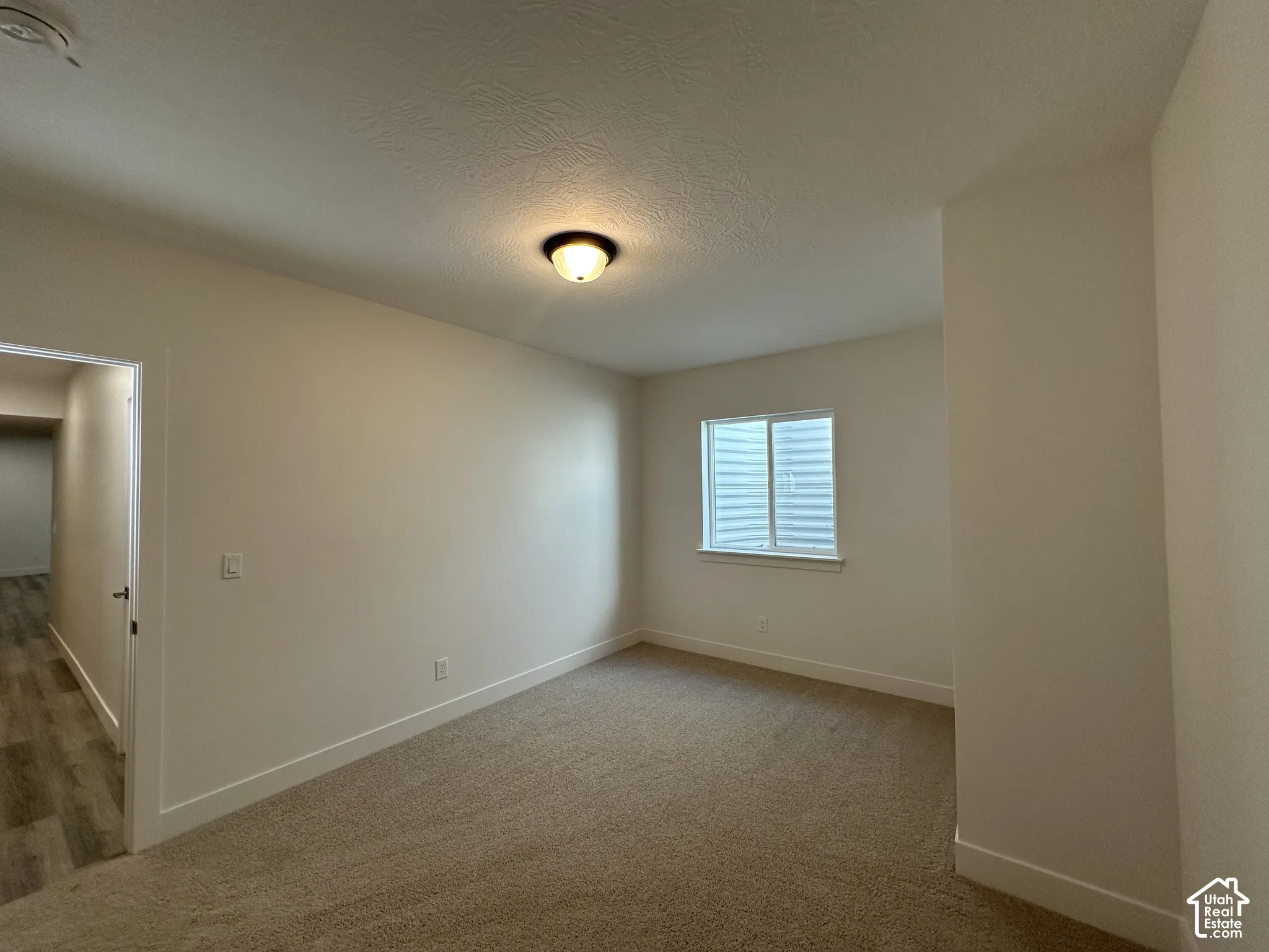 Carpeted room featuring a single window with blinds, a ceiling-mounted light fixture, and white painted walls with matching baseboards