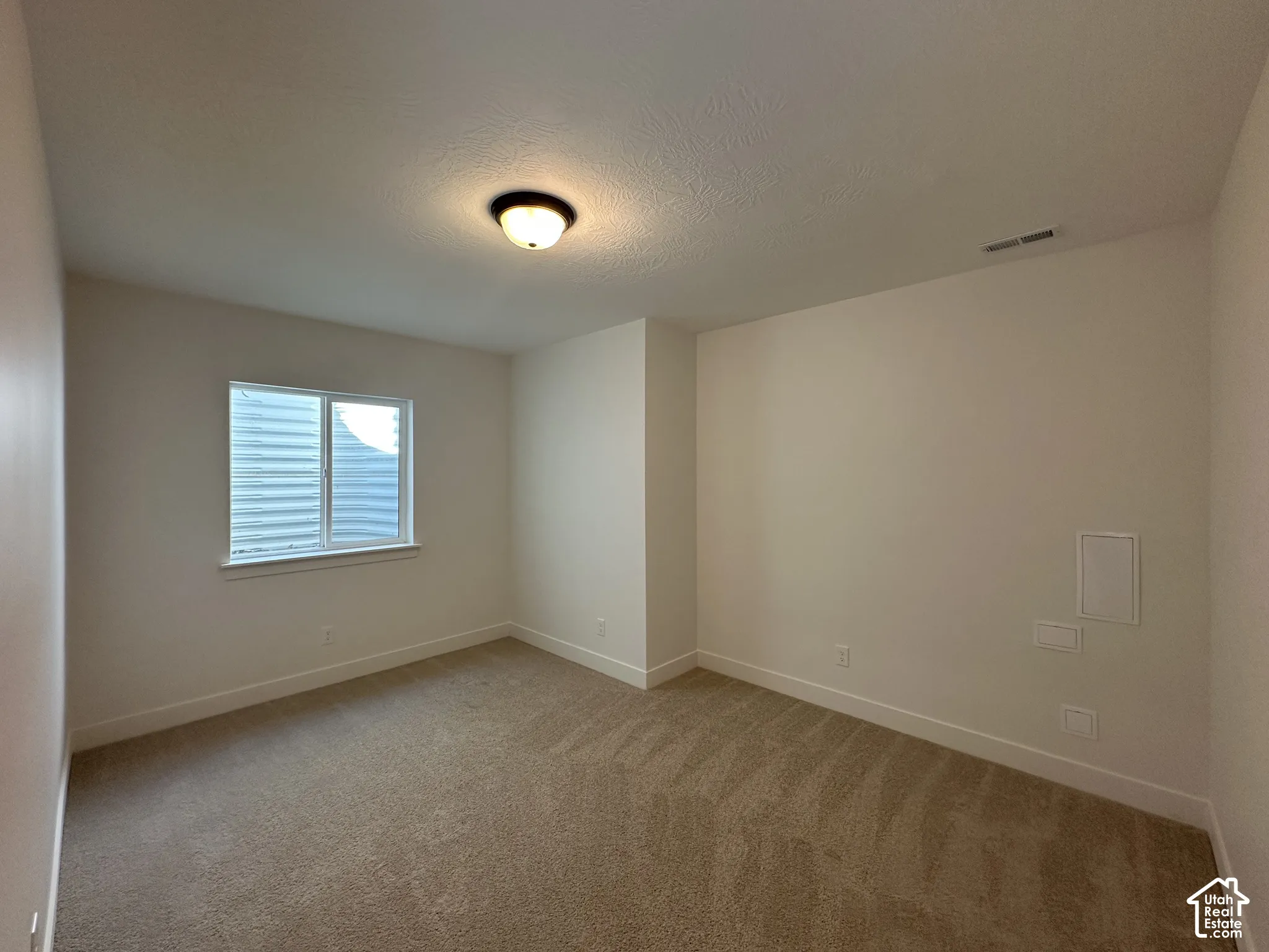 Bright secondary bedroom featuring neutral wall finishes, wood-finish flooring, and a large window with plantation shutters providing natural light