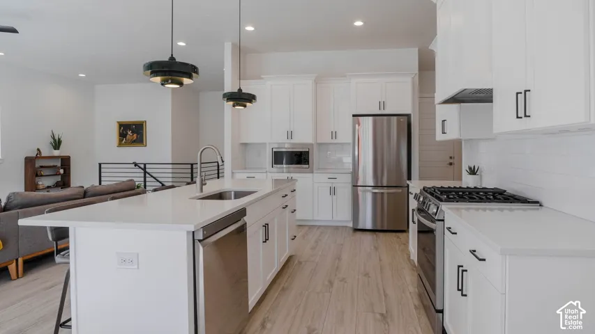 Kitchen featuring a large center island with integrated sink, white cabinetry with dark hardware, stainless steel appliances, and light wood-finish flooring