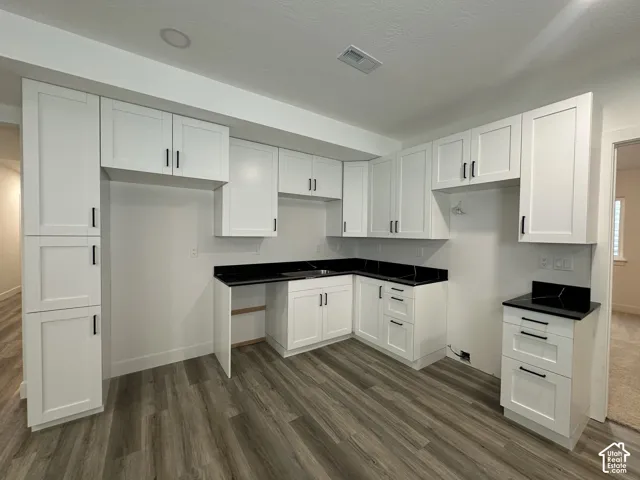Bright kitchen featuring white shaker-style cabinetry with chrome hardware, black wood-finish countertops, and an open layout with multiple work zones