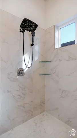 Walk-in shower featuring large format white tile walls with grey veining, a black multi-function showerhead with handheld sprayer, chrome fixtures, two clear glass corner shelves, and a square window