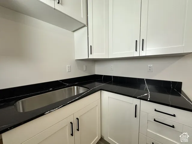 Modern kitchen or utility space featuring white shaker-style cabinetry with matte black hardware, black countertops with white veining, and an undermount stainless steel sink
