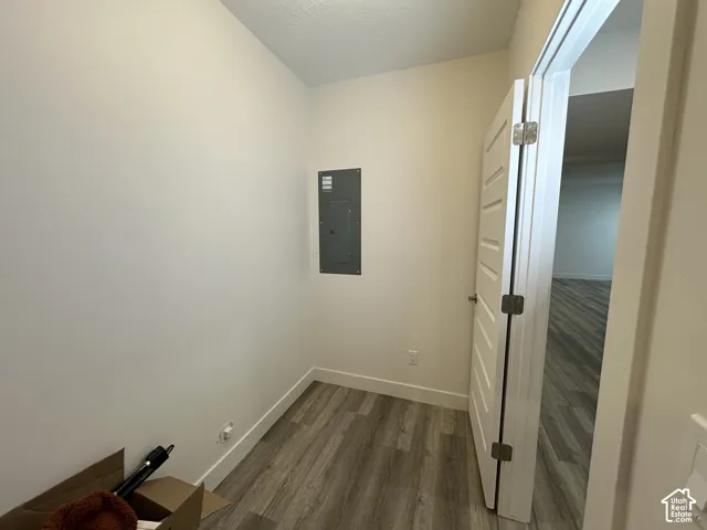 Compact utility space featuring light-toned walls, wood-finish flooring, a white five-panel door, and a visible electrical panel