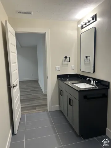 Bathroom vanity with a dark countertop and integrated sink, gray cabinetry, and a rectangular mirror with a black frame