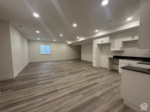 Spacious interior featuring wood-finish flooring, recessed lighting, and a kitchen area with white cabinetry and dark countertops
