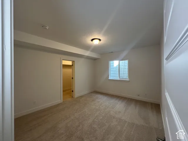 Spacious room featuring neutral carpeting, a ceiling-mounted light fixture, and a window with blinds