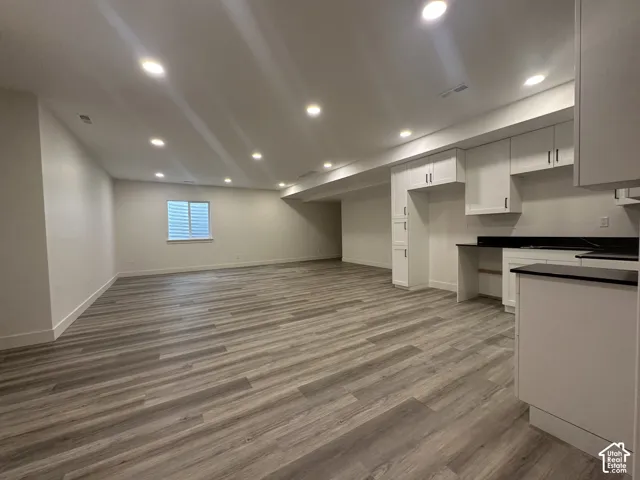 Spacious open-concept area featuring wood-finish flooring, recessed lighting, and a kitchen area with white cabinetry and dark countertops