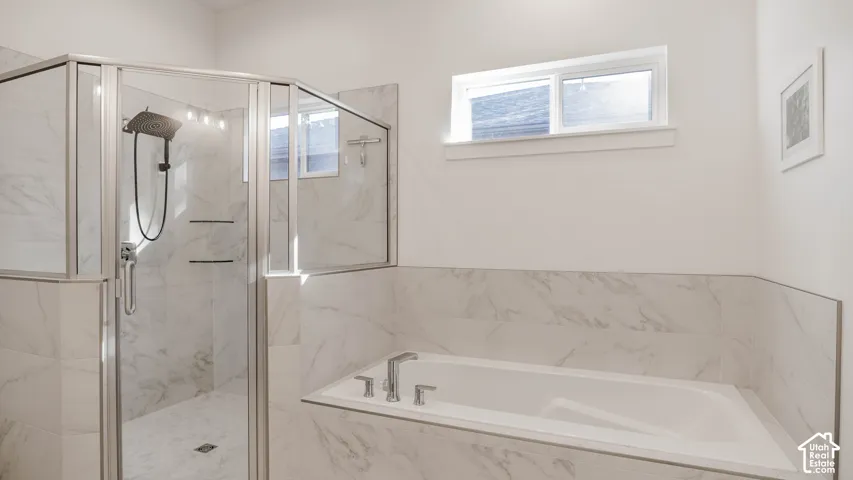 Bright bathroom featuring a spacious walk-in shower with glass enclosure, an integrated bathtub, and white marble-look tile surrounds