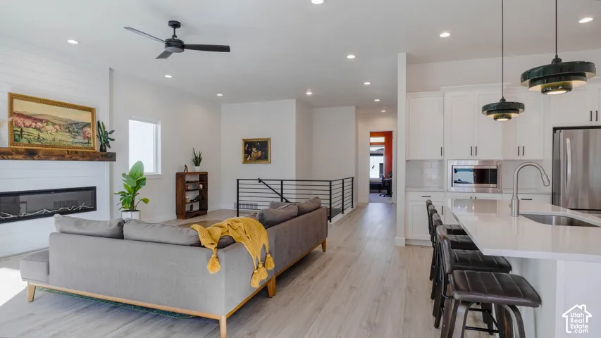 Open-concept living space featuring wood-finish flooring, a contemporary linear fireplace with a wood mantel, and an adjacent kitchen with white cabinetry