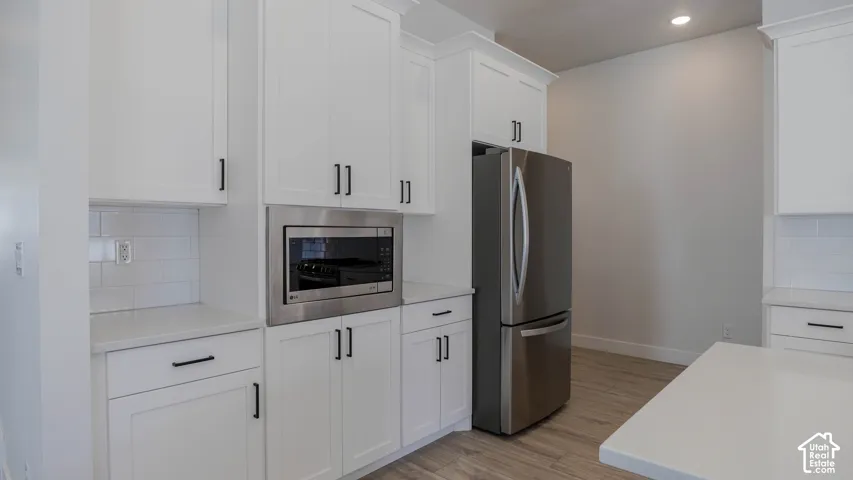 Kitchen featuring white shaker cabinetry, stainless steel appliances, light countertops, subway tile backsplash, and wood-finish flooring