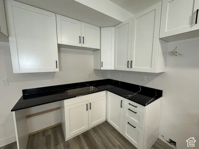 White shaker-style cabinetry with matte black hardware, dark countertops with white veining, integrated stainless steel sink, and wood-finish flooring