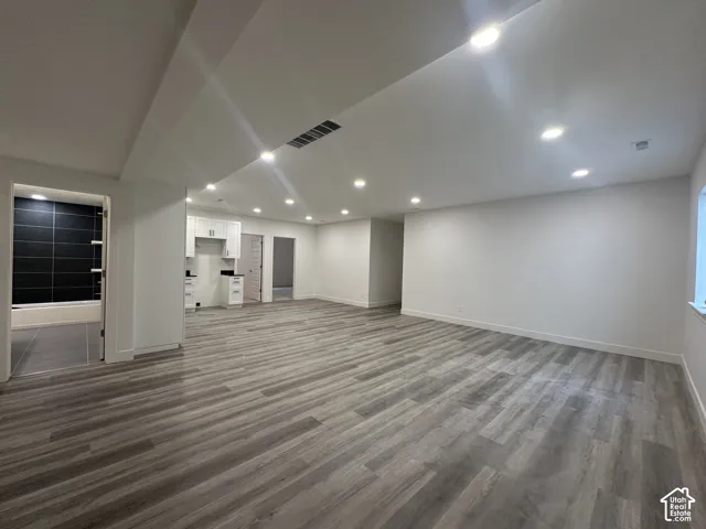 Spacious interior featuring wood-finish flooring, recessed lighting, and a white cabinet kitchenette with a dark countertop