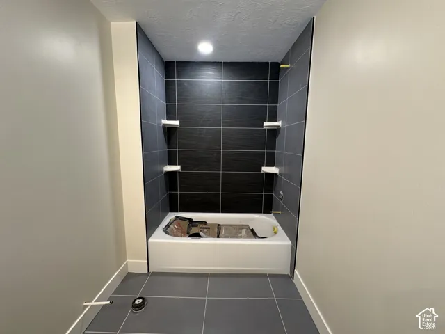 Bathroom featuring a white bathtub, dark gray tile surround, recessed lighting, and built-in shelving