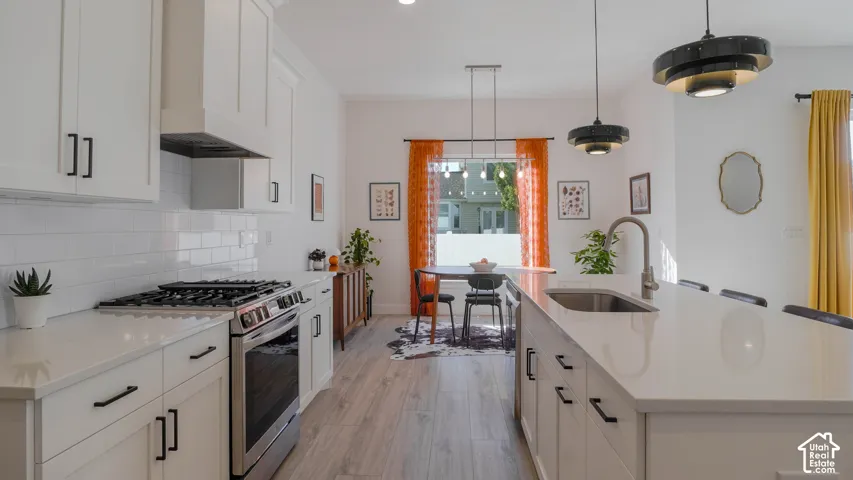 Gourmet kitchen with white shaker cabinetry, stainless steel appliances, a subway tile backsplash, and a large island featuring a stainless steel sink and modern pendant lighting