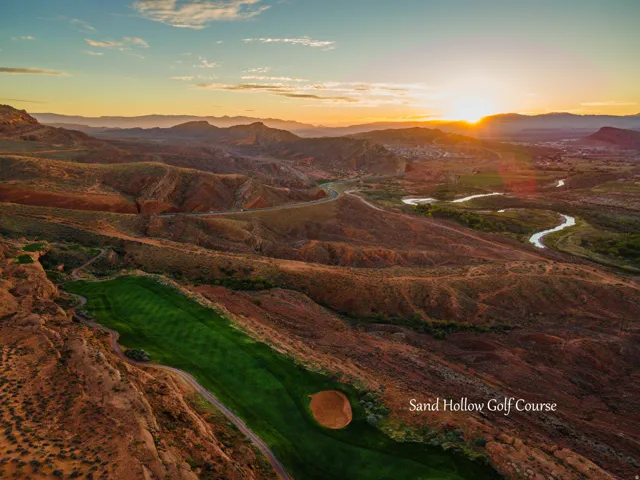 Aerial view of Sand Hollow Golf Course showcasing dramatic desert terrain with layered earth tones, winding water features, manicured fairways, and expansive mountain vistas at golden hour