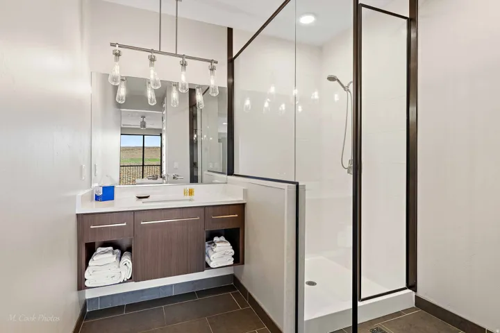 Modern primary bathroom featuring a wood-finish vanity with dual storage cubbies, white quartz countertop, and chrome vessel sink