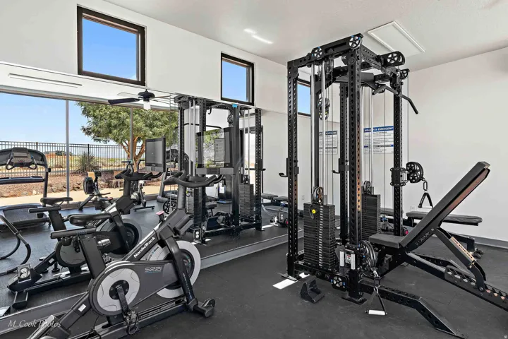 Dedicated fitness room featuring rubberized flooring, a full-length mirrored wall, a ceiling fan, and upper transom windows