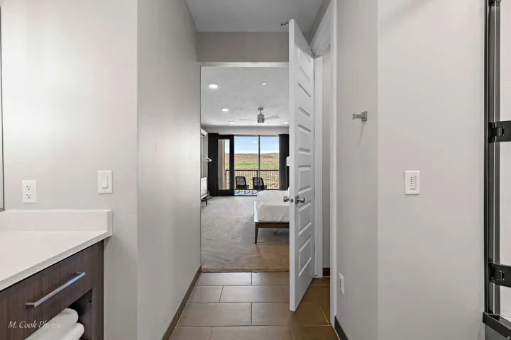 Transitional hallway with ceramic tile flooring leading to a bedroom featuring a contemporary ceiling fan, large windows, and a private balcony