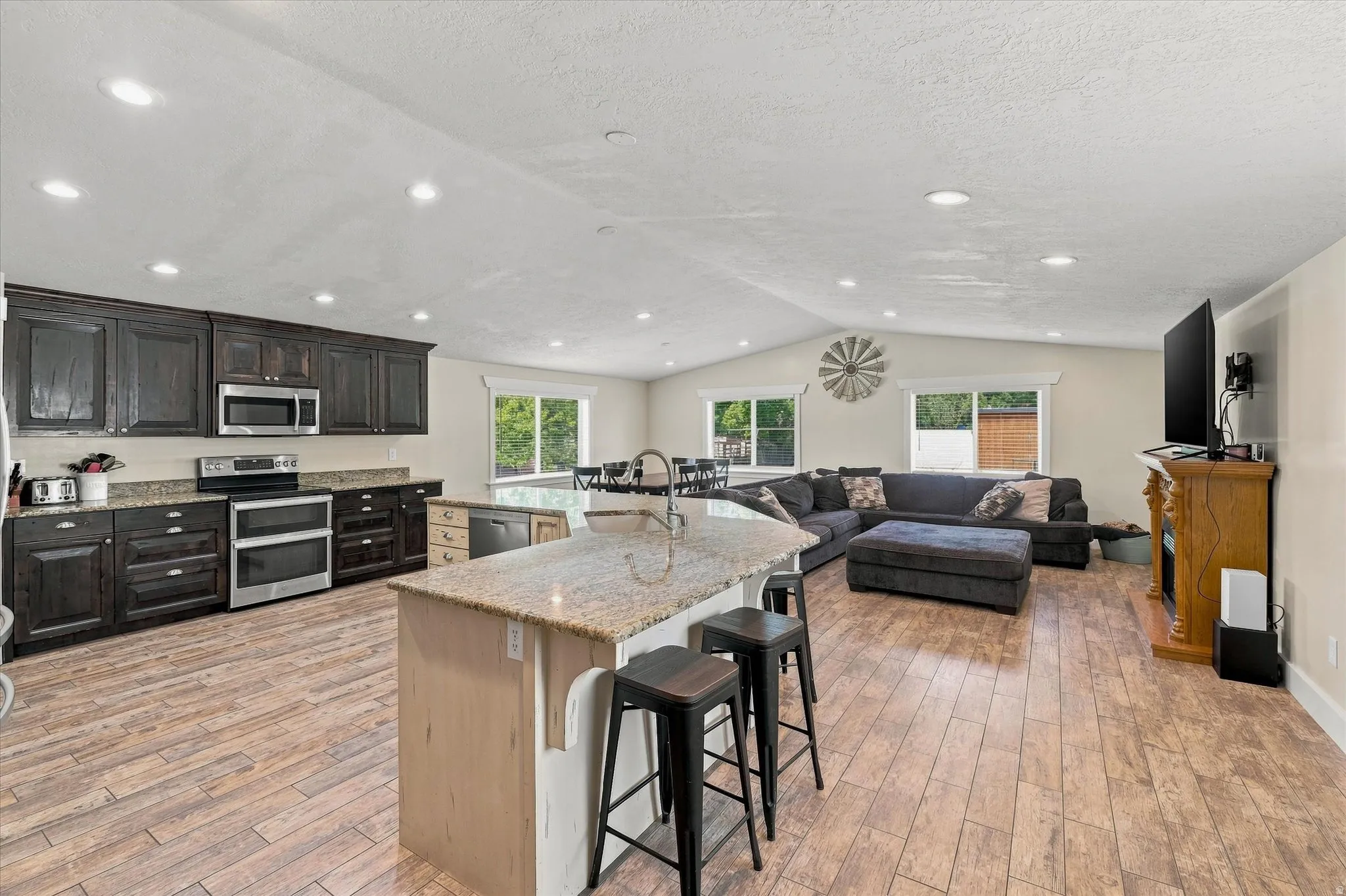 Expansive open-concept living space featuring wood-finish flooring, a vaulted ceiling with recessed lighting, and multiple windows