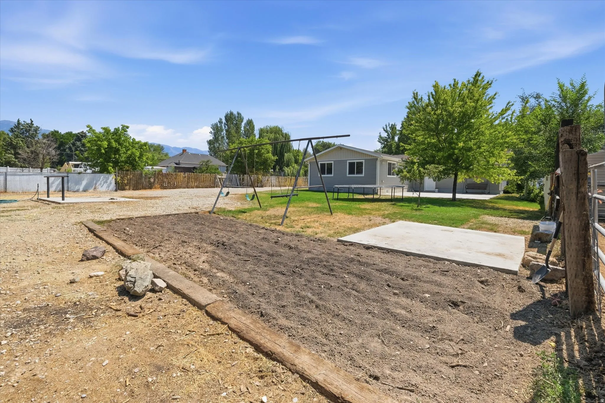 Expansive backyard featuring a large tilled garden area, a concrete pad, and a separate grassy area