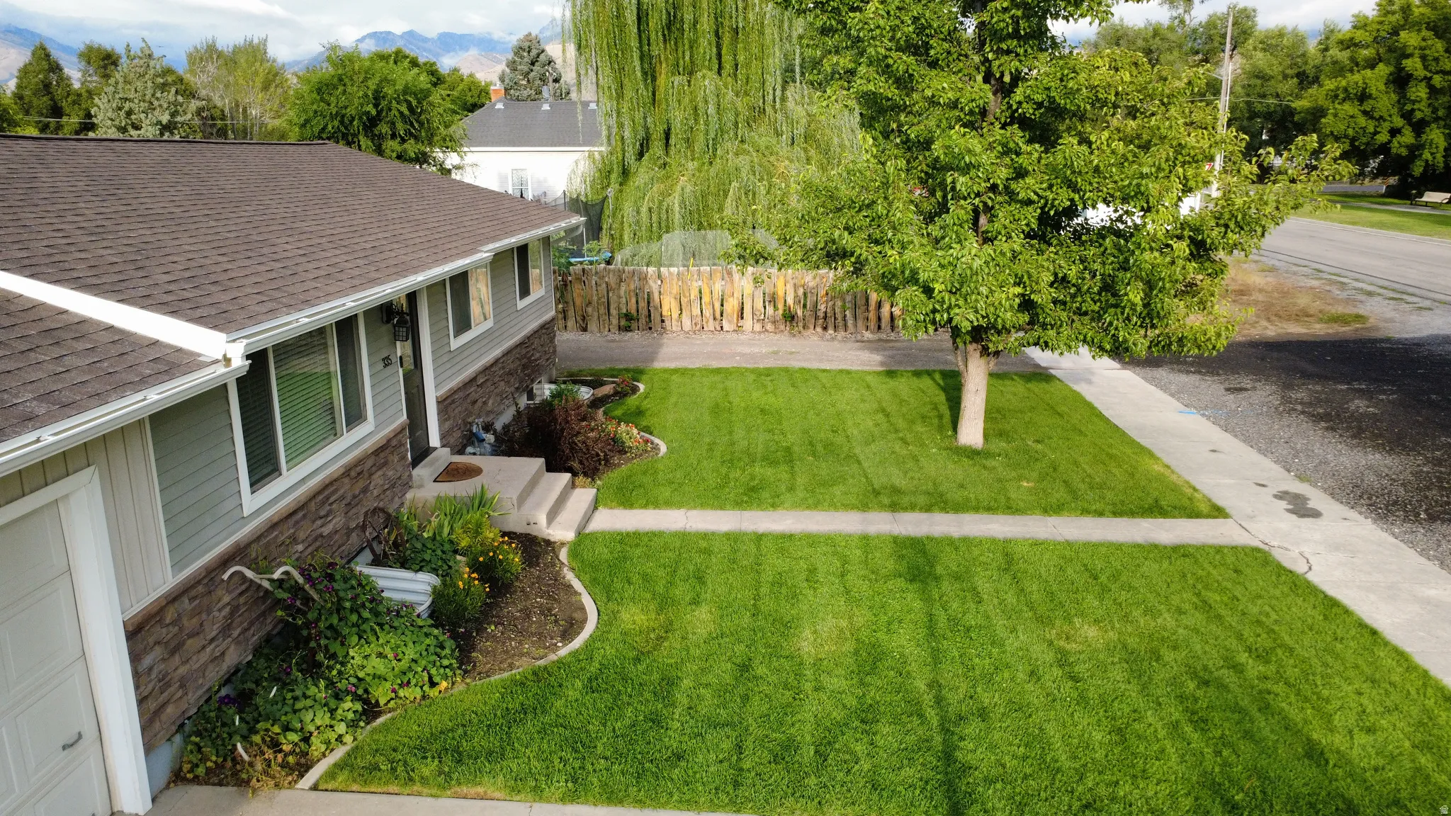 Exterior featuring gray siding, a stone veneer accent, a brown shingle roof, and a front entry with concrete steps