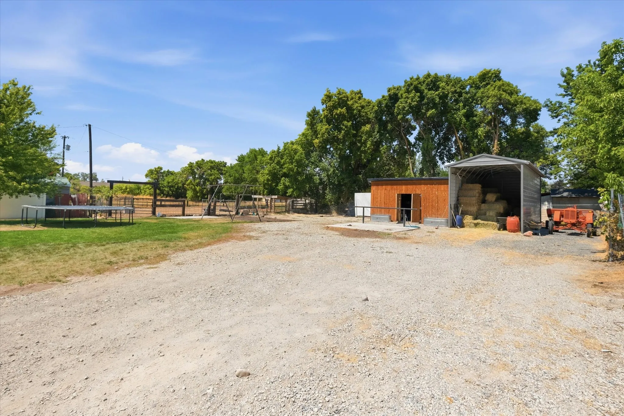 Expansive gravel parking area fronting a wood-sided outbuilding and a metal-roofed open-sided storage structure