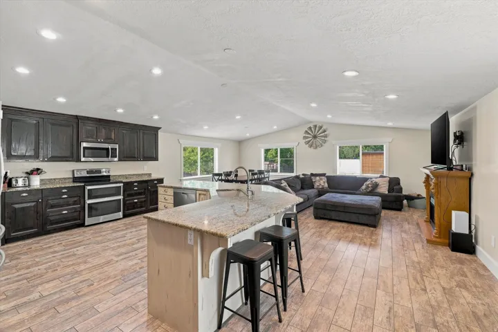 Expansive open-concept living space featuring wood-finish flooring, a vaulted ceiling with recessed lighting, and multiple windows