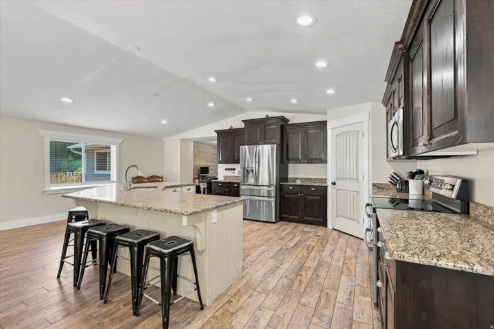 Spacious kitchen featuring an expansive island with a stone-finish countertop, dark wood cabinetry, stainless steel appliances, recessed lighting, and wood-finish flooring