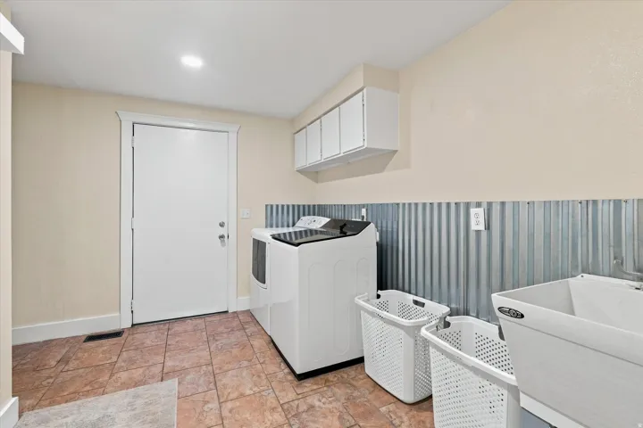 Dedicated laundry space featuring a utility sink, upper cabinetry, and a corrugated metal accent wall