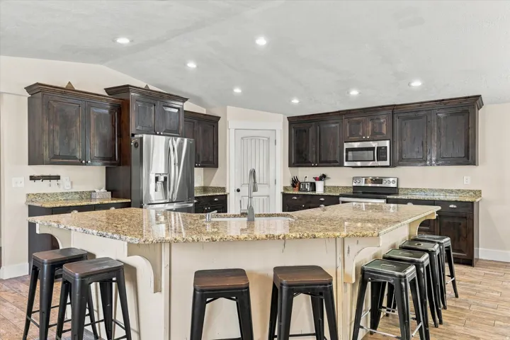 Spacious kitchen featuring dark wood cabinetry, granite countertops, stainless steel appliances, a large central island with seating, and recessed lighting