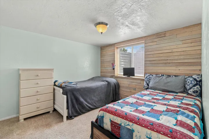 Comfortable bedroom featuring dual beds with coordinating bedding, wood-finish accent wall, carpeted flooring, four-drawer dresser with ample storage, and recessed ceiling lighting