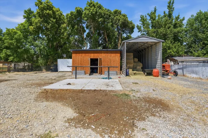 Rural property featuring functional outbuildings including a wood-finish storage structure with open shelving and a metal-clad equipment shed