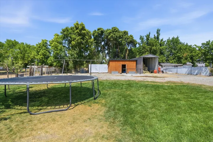 Spacious recreational property featuring a large manicured lawn with mature shade trees, a trampoline, and multiple outbuildings including an orange storage shed and metal structures