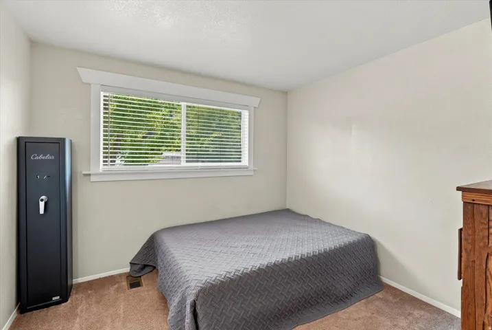 Comfortable bedroom featuring a large window with horizontal blinds providing natural light and privacy, wood-finish flooring, neutral wall finishes.