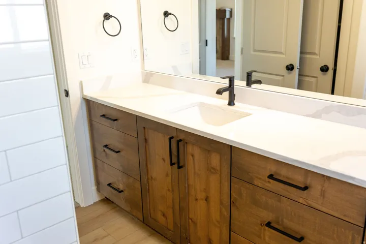 Elongated vanity featuring wood-finish cabinetry with matte black hardware
