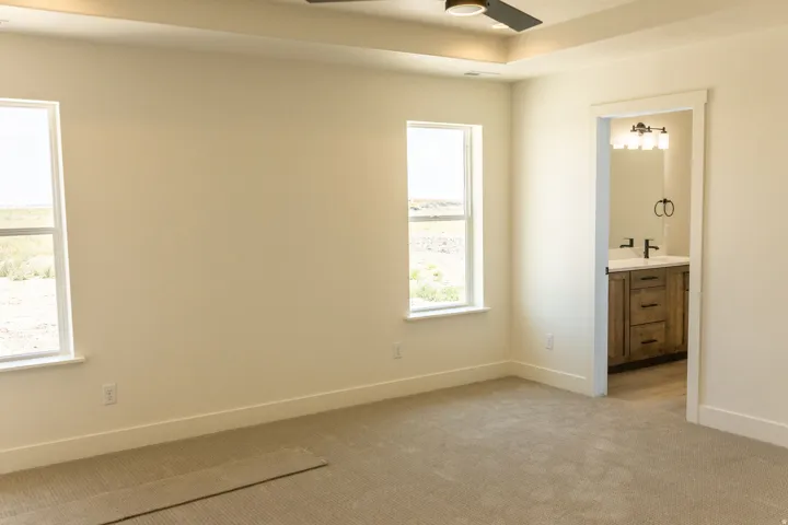 Recessed ceiling with an integrated fan, dual windows, plush carpeting, and a separate doorway to a vanity with a white countertop
