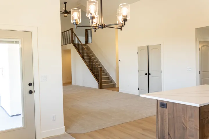 Vaulted ceilings with chandelier lighting, wood-finish flooring, staircase with dark wood banister, light-colored carpeting, and a kitchen island with a light-colored countertop