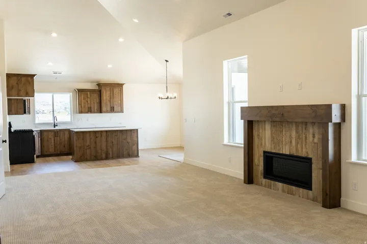 Vaulted ceiling with recessed lighting, integrated kitchen island with a stone-finish countertop, wood-finish cabinetry, built-in fireplace, and expansive carpeting