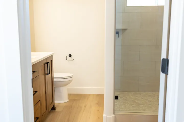 Wood-finish flooring, wood vanity with black hardware, white countertop, and tiled shower with glass enclosure