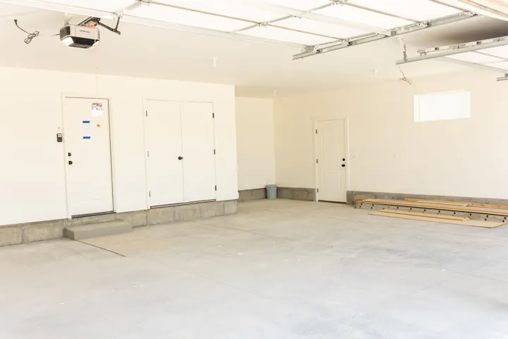 Spacious garage with light-toned concrete flooring, white painted walls, and a visible garage door opener mechanism