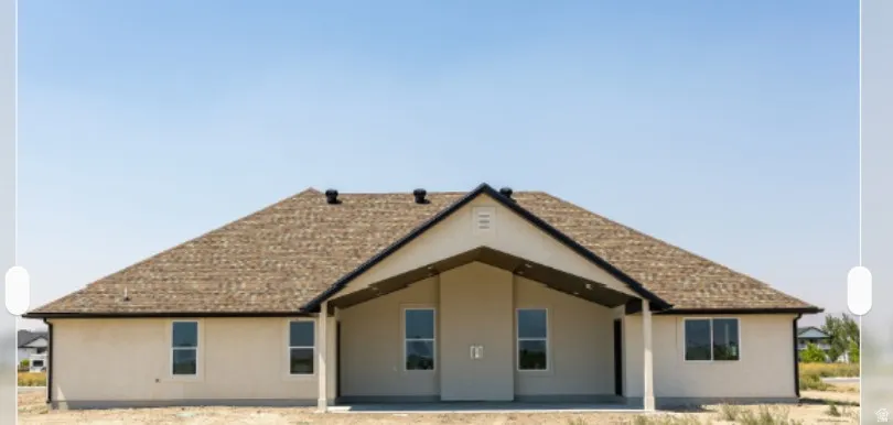 Exterior featuring a light stucco finish, brown shingle roofing, and a prominent covered patio area