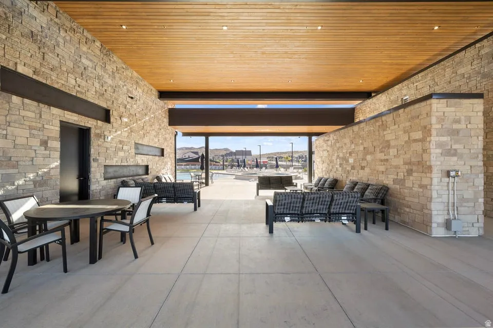 Expansive covered patio featuring stone veneer walls, wood-finish ceiling with recessed lighting, and large format concrete-style flooring