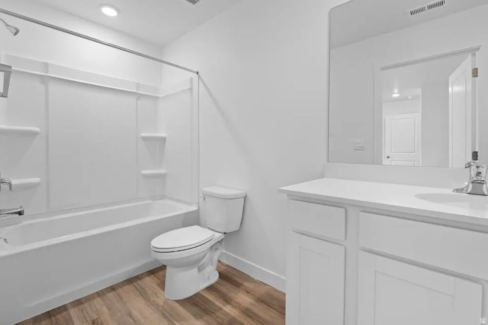 Bathroom featuring a white tub/shower combination, a white toilet, and wood-finish flooring