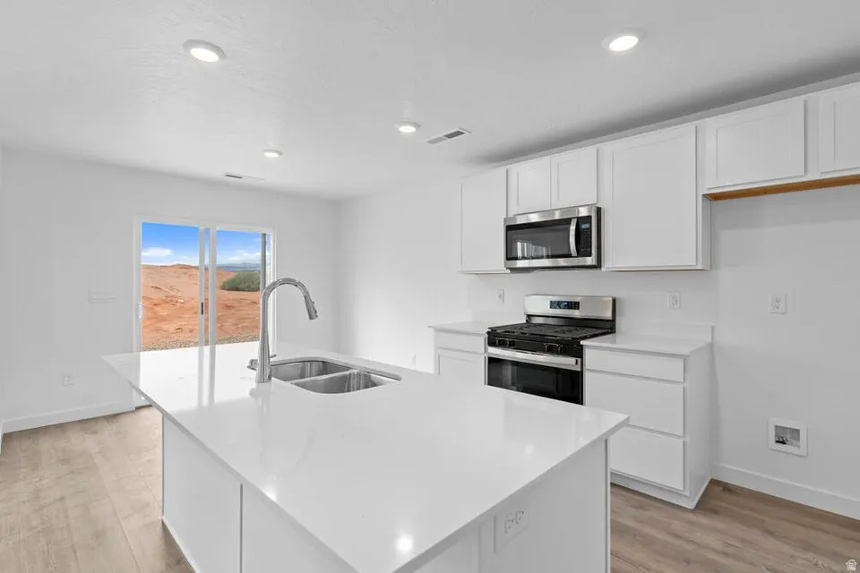 Modern kitchen featuring an island with a double basin sink, white cabinetry, integrated stainless steel appliances, white countertops, and wood-finish flooring