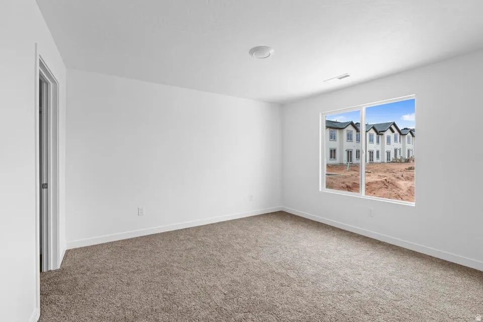 Bright room featuring a large window, neutral carpeting, white walls, and a flush-mount ceiling light